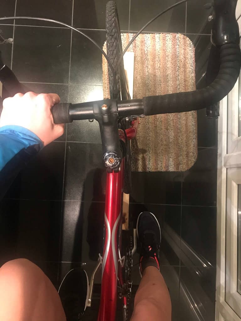 Woman's left hand gripping handlebar of red Raleigh bicycle with feet on pedals in a kitchen 