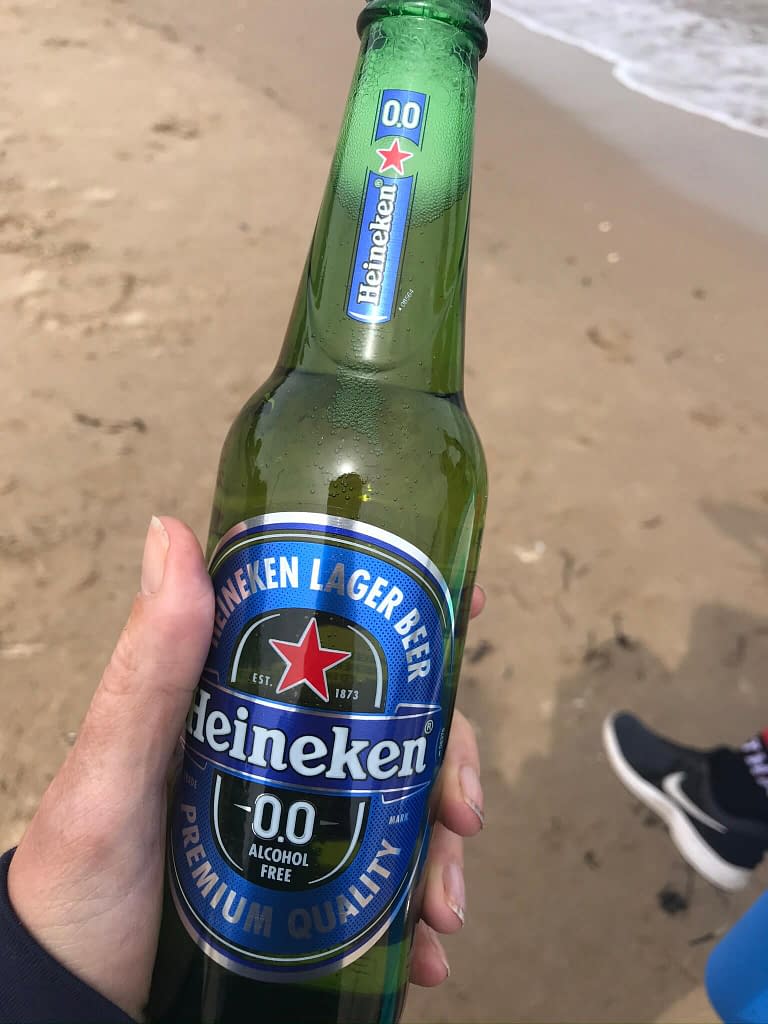 Woman's hand holding a glass bottle of Heineken Zero beer on a beach 