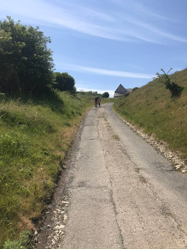 Man in pink shorts pushing a mountain bike up road on a steep hill towards Worth Matravers on the Isle of Purbeck