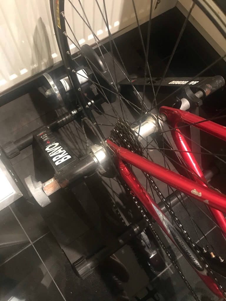 Close up of back wheel of red Raleigh bike on a turbo trainer showing the cylinder the tyre spins on 