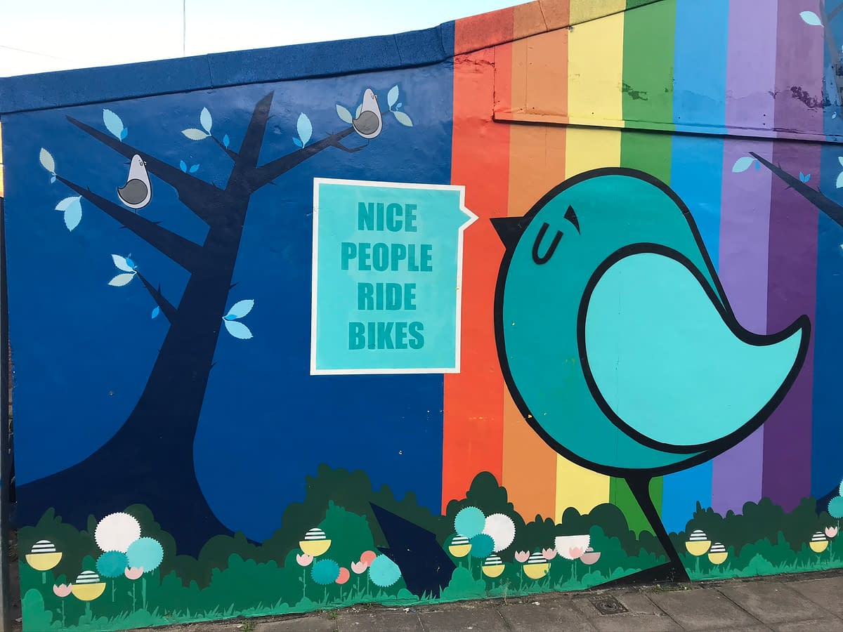 Mural with tree birds and rainbow with a sign that says 'nice people ride bikes'
